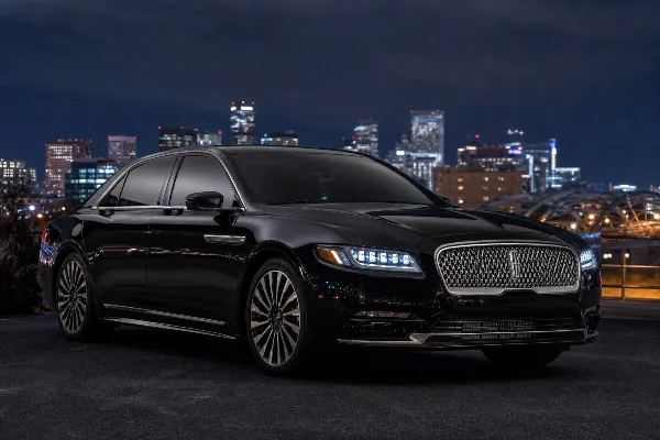 A black luxury sedan parked in front of a city skyline at night.
