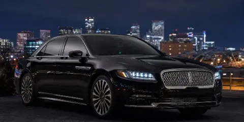 A black luxury sedan parked in front of a city skyline at night.