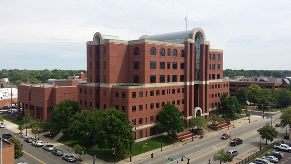 Aerial view of the Sangamon County Courts Complex, a multi-story red brick building with a central glass atrium, surrounded by trees and parking areas.