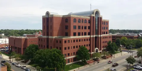 Aerial view of the Sangamon County Courts Complex, a multi-story red brick building with a central glass atrium, surrounded by trees and parking areas.