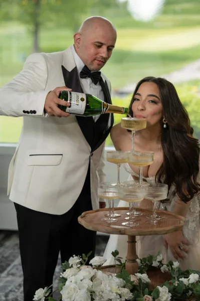 A couple at a wedding event with a man pouring champagne into a tiered glass tower.