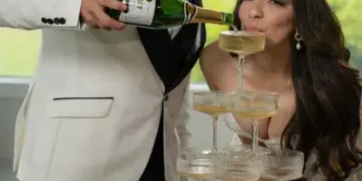 A couple at a wedding event with a man pouring champagne into a tiered glass tower.