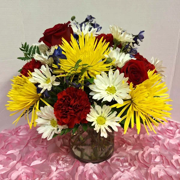 Mixed bouquet of red roses, yellow spider mums, and white daisies in a glass vase