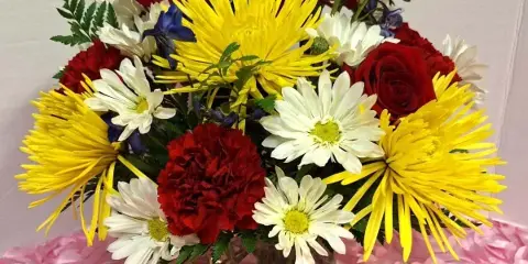 Mixed bouquet of red roses, yellow spider mums, and white daisies in a glass vase