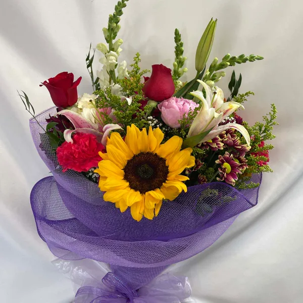 A mixed floral bouquet containing a sunflower, red roses, and lilies, wrapped in purple mesh.
