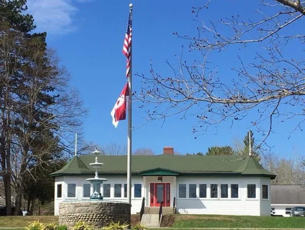 Exterior view of the Waldo County Shrine Club building with a green roof, white siding, red front door, and a flagpole with the American flag and a red flag.