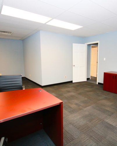 Interior view of a furnished office space with a red desk, gray chair, and light blue walls.