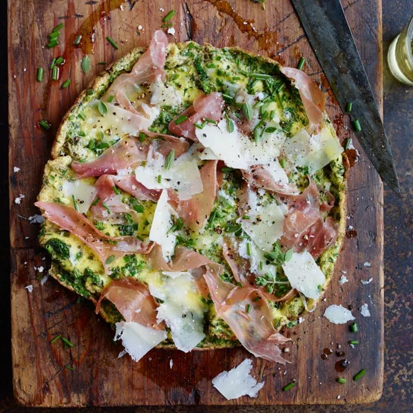 A prepared catering dish featuring focaccia topped with prosciutto, cheese, and herbs on a wooden cutting board.