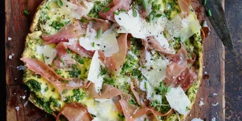 A prepared catering dish featuring focaccia topped with prosciutto, cheese, and herbs on a wooden cutting board.