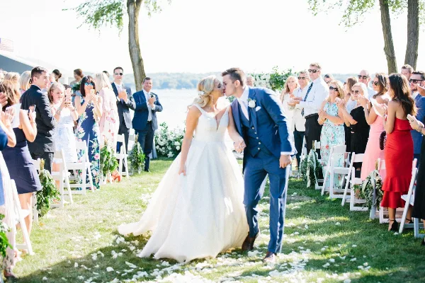 A bride and groom kissing as they walk down the aisle during an outdoor wedding ceremony.