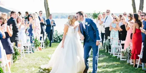 A bride and groom kissing as they walk down the aisle during an outdoor wedding ceremony.