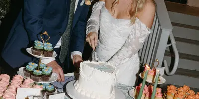Bride and groom cutting a wedding cake at a decorated table outdoors at a historic mansion venue.