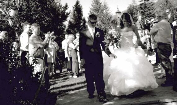 A bride and groom walking down the aisle during an outdoor wedding ceremony with guests seated on either side.