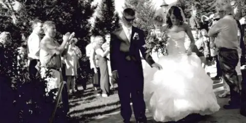 A bride and groom walking down the aisle during an outdoor wedding ceremony with guests seated on either side.