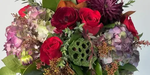 A floral arrangement with red roses, purple hydrangeas, and dark chrysanthemums in a galvanized metal bucket.