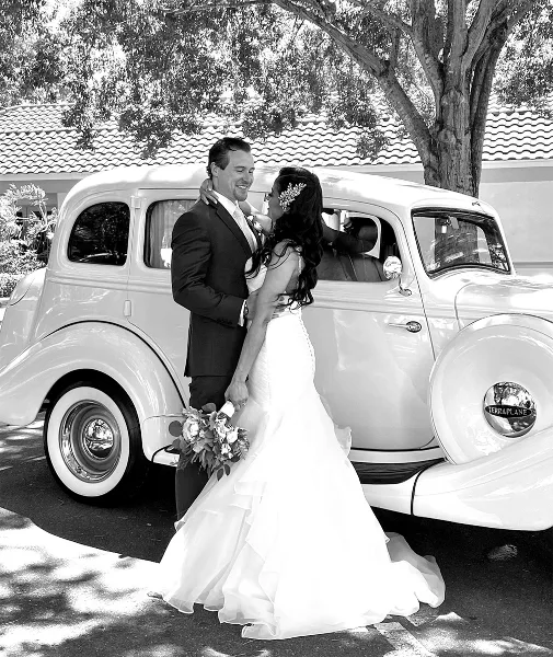 A bride and groom posing with a white 1935 Hudson Terraplane vintage car.