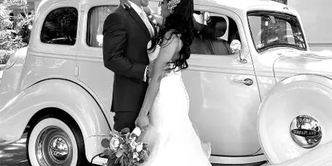 A bride and groom posing with a white 1935 Hudson Terraplane vintage car.