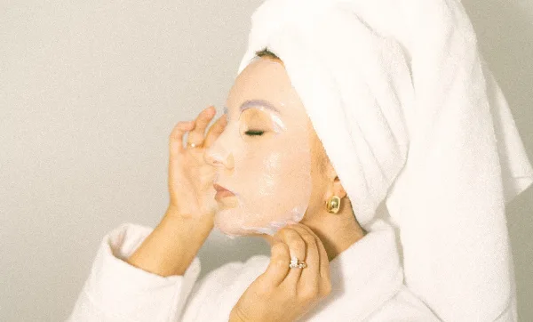 Woman with a towel on her head and a sheet mask on her face during a skincare treatment