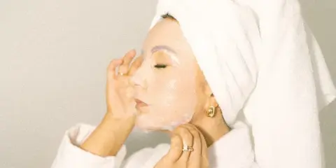 Woman with a towel on her head and a sheet mask on her face during a skincare treatment