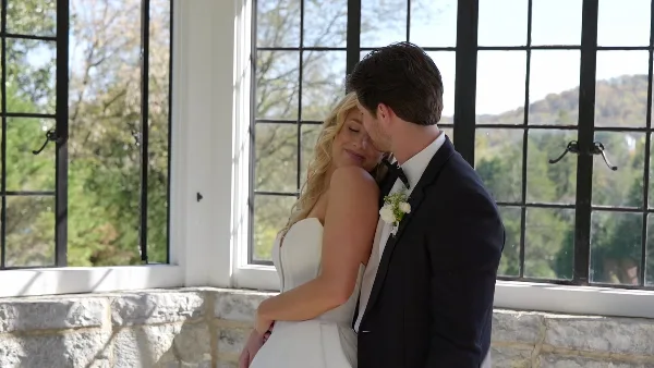 A bride and groom embracing in a sunlit room with large windows, captured in a cinematic wedding video style.