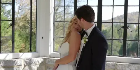 A bride and groom embracing in a sunlit room with large windows, captured in a cinematic wedding video style.