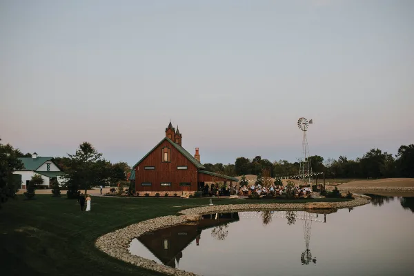 Exterior view of the Thunderhead Pines venue featuring a red barn-style building, a windmill, and a lake at dusk.