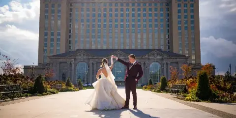 A bride and groom dancing in front of a large, historic building with a stone facade.