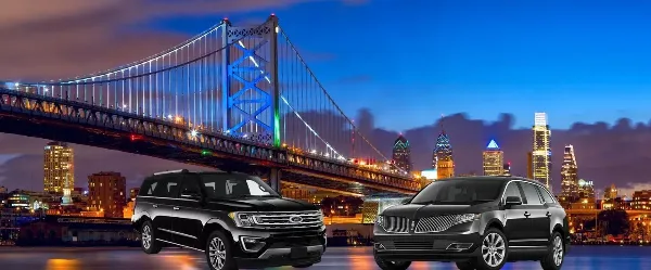 Two black luxury SUVs parked in front of a city skyline and bridge at night.
