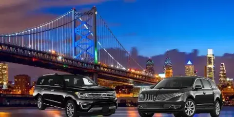 Two black luxury SUVs parked in front of a city skyline and bridge at night.