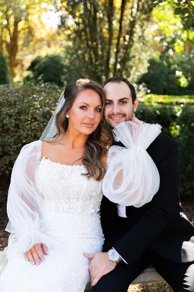 A professional color photograph of a bride and groom posing together outdoors in a garden setting.
