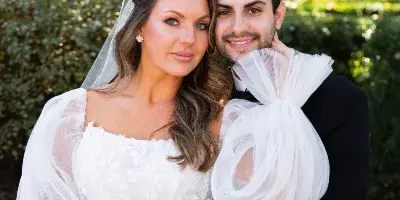 A professional color photograph of a bride and groom posing together outdoors in a garden setting.