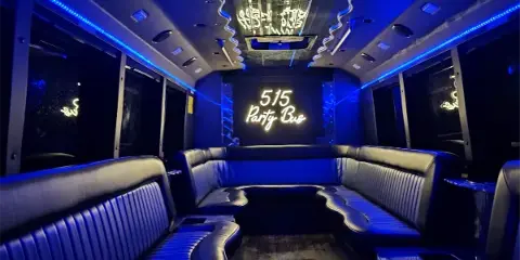 Interior view of a party bus with blue LED lighting, black leather bench seating, and a neon sign reading '515 Party Bus'.