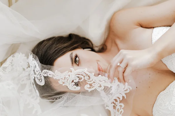 Close-up portrait of a bride with styled hair and makeup, partially covered by a lace veil.
