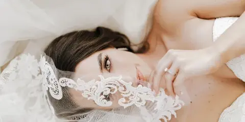 Close-up portrait of a bride with styled hair and makeup, partially covered by a lace veil.