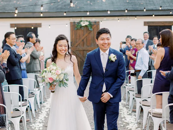 A bride and groom walking down the aisle during a wedding ceremony while guests applaud.