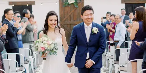 A bride and groom walking down the aisle during a wedding ceremony while guests applaud.