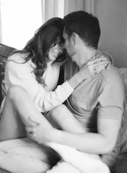 A black-and-white film photograph of a couple sharing an intimate, smiling moment while sitting on a couch.