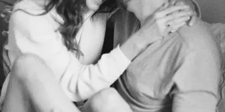 A black-and-white film photograph of a couple sharing an intimate, smiling moment while sitting on a couch.
