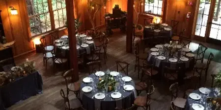 An overhead view of a rustic wooden event hall set up for a wedding reception with round tables, dark linens, and place settings.