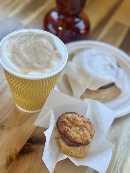 A cup of coffee, a scone with cream, and a muffin on a wooden table.