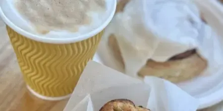 A cup of coffee, a scone with cream, and a muffin on a wooden table.
