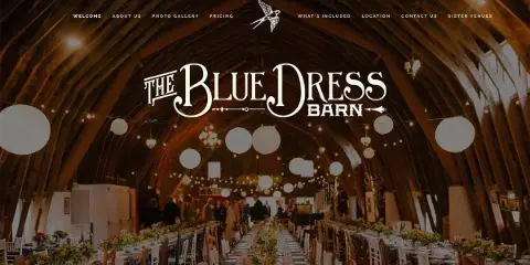 Interior view of a wedding barn venue with a high wooden ceiling, string lights, and long tables set for a reception.