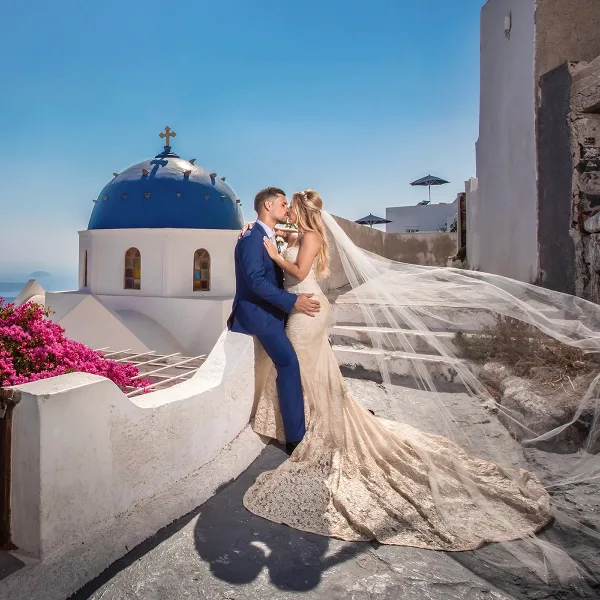 A bride and groom sharing a kiss in front of a blue-domed church in Santorini.