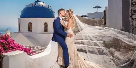 A bride and groom sharing a kiss in front of a blue-domed church in Santorini.