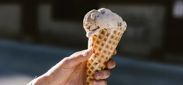 A hand holding a waffle cone with a scoop of ice cream.