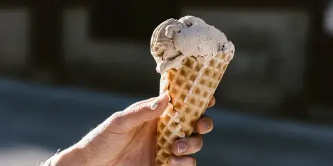 A hand holding a waffle cone with a scoop of ice cream.