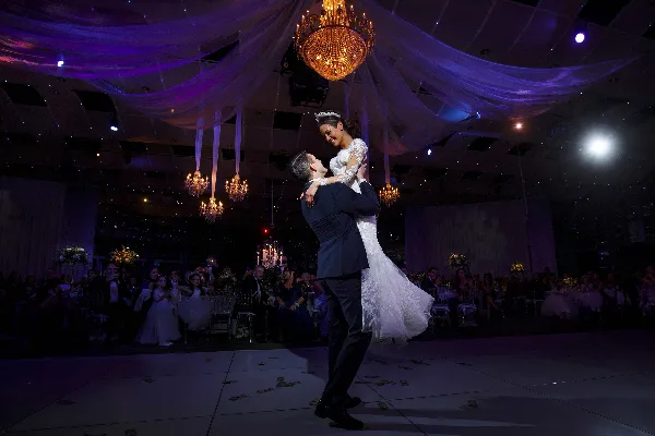 A bride and groom dancing during their wedding reception under a chandelier and draped fabric.