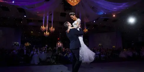 A bride and groom dancing during their wedding reception under a chandelier and draped fabric.