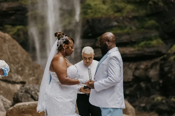 A wedding officiant performing a ceremony for a couple at a waterfall.