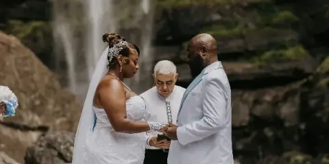 A wedding officiant performing a ceremony for a couple at a waterfall.